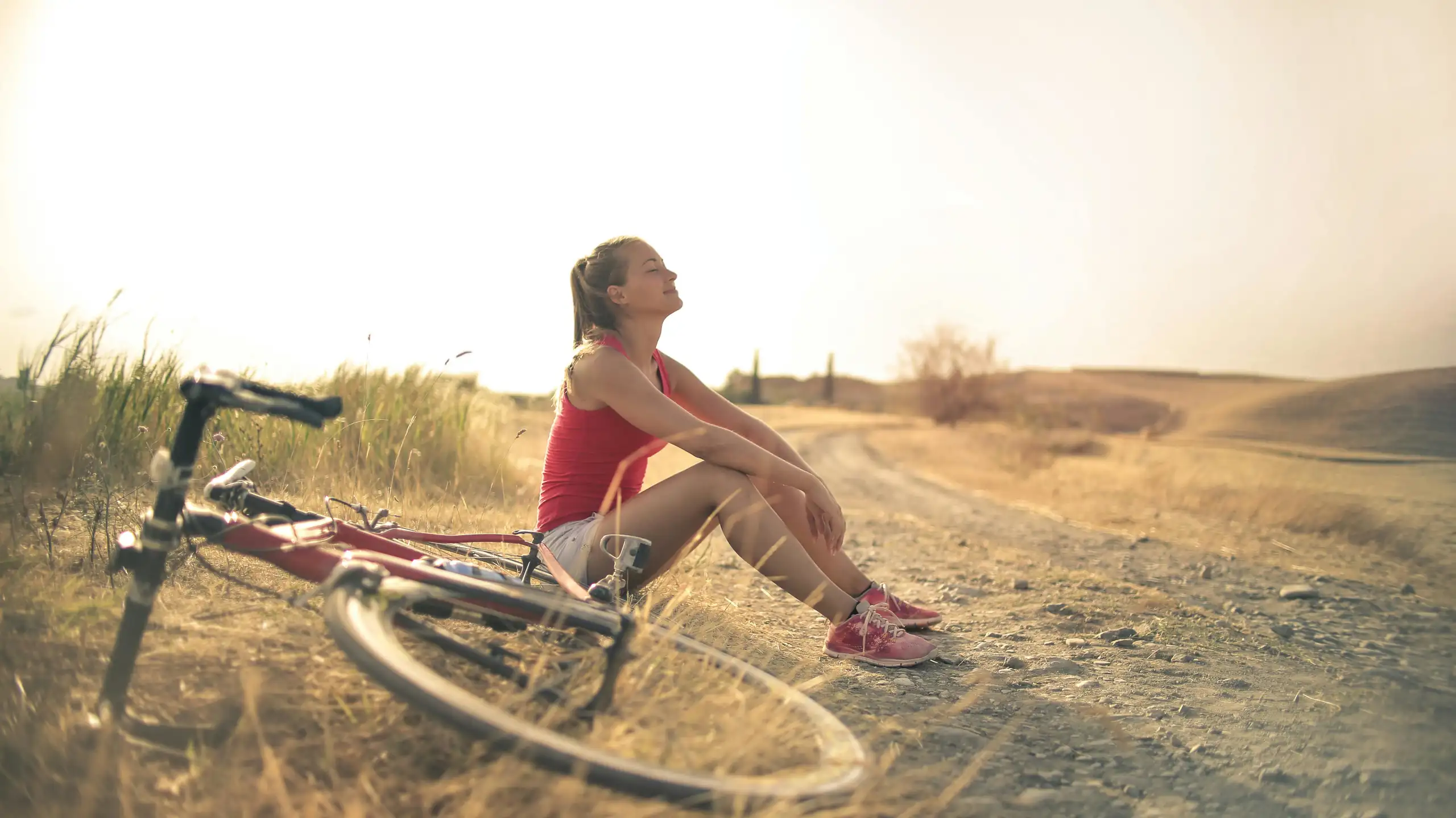 A woman sitting smiling beside her bicycle.